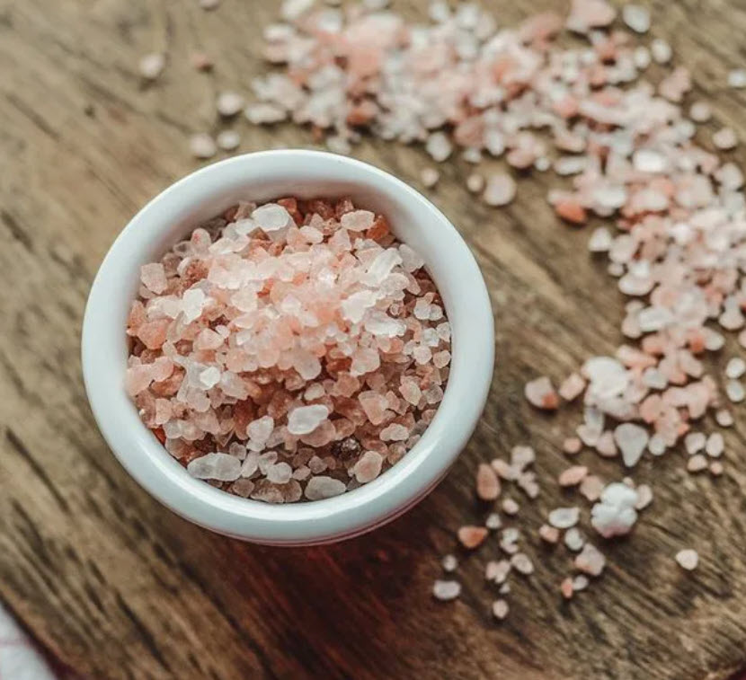 A bowl of pink salt sitting on top of a wooden table.